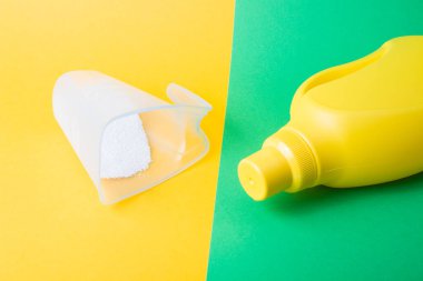 Çocuk giysilerini yıkamak için jel ve çamaşır tozu ile ölçme kabı ile sarı-yeşil arka plan fotokopi alanı üzerinde uzanan sarı plastik şişe.