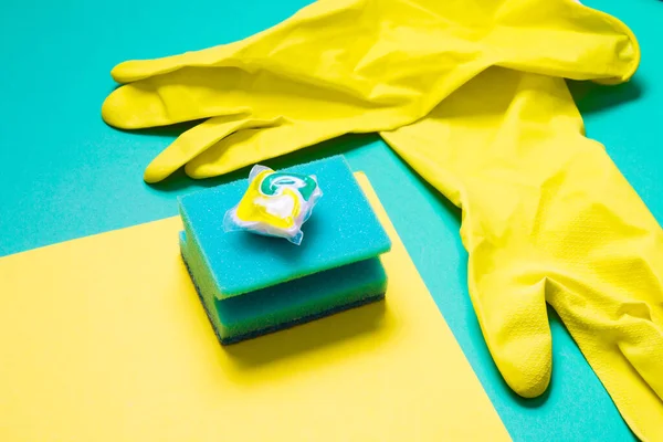 yellow rubber gloves, gel capsules for dishwashers and sponges on a green and yellow background, places of the copy top view, the choice between washing dishes or in the dishwasher