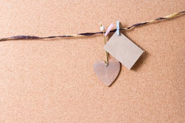 Küçük bir parça kahverengi el işi kâğıdı ve kalp şeklinde tahta bir Noel ağacı oyuncağı mantar tahtasında küçük ahşap mandalları olan bir ipe asılı.