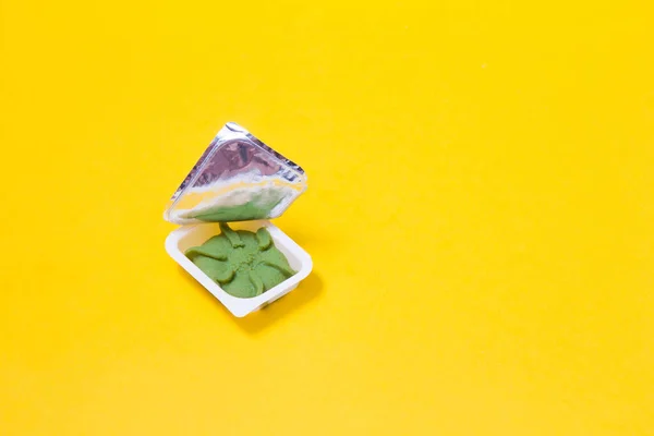 wasabi in a small plastic container for home delivery of rolls and sushi, yellow background copy space, open packaging of wasabi sauce
