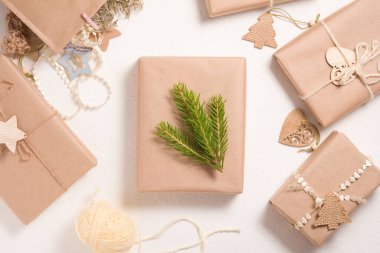 Beyaz arka planda çevre dostu hediye kutuları, ahşap figürler ve doğal malzemelerle süslenmiş hediyeler, ladin dallarıyla süslenmiş bir kutu.