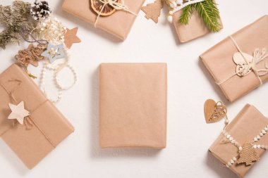 Beyaz arka planda çevre dostu birkaç Noel hediyesi kutusu, ahşap Noel ağacı oyuncakları, kurutulmuş portakal ve ladin dalları,