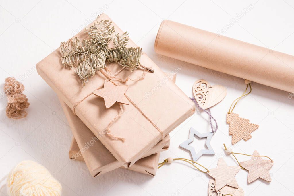 eco friendly gift box packaging for christmas or new year, wooden christmas toys, box wrapped in kraft paper with a spruce branch and a wooden star on a white background