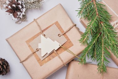 Eko kağıdına sarılı hediye kutusu ve ev yapımı etiketlerle süslenmiş bir Noel ağacı ahşap heykeli, doğal ladin dalları ve çevre stili hediyeler için çam kozalakları.