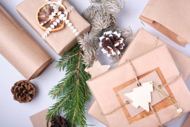 Ekolojik kağıda paketlenmiş hediye kutuları, DIY hediyeleri için doğal süslemeler, köknar dalları, koniler ve dekorasyon için ahşap heykelcikler, üst manzara, gri arka plan, sıfır atık yaşam tarzı.