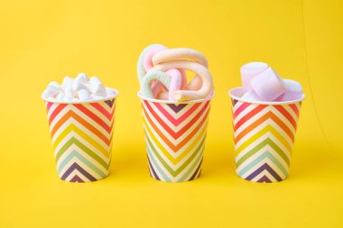 Sarı arka planda geometrik desenli, bayramlık kağıt bardaklarda farklı tipte şekerlemeler, boşluğu kopyala