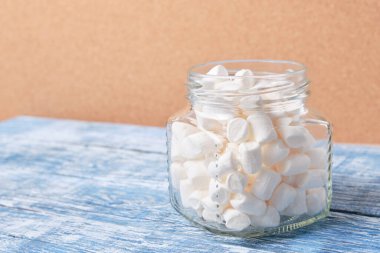 Dekorasyon ve içecek için küçük beyaz şekerlemeler ve ahşap mavi arka planda bir kavanozda kek süslemesi.