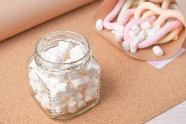 small white marshmallows for decoration and drink and decoration of cakes in a jar against the background of a cork board and a bag with long spaghetti marshmallows, copy space