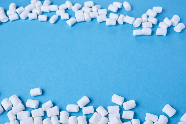 small white marshmallows are scattered on a blue background copy space, focus at the bottom of the image, marmalade frame