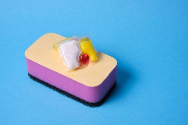 Bulaşık makineleri için jel kapsülleri ve süngerler, fotokopi makinesinin bulunduğu yerin yeşil ve sarı arka planında, bulaşık yıkama ile bulaşık makinesi arasında seçim