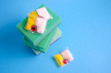 Bulaşık makineleri için jel kapsülleri ve süngerler, fotokopi makinesinin bulunduğu yerin yeşil ve sarı arka planında, bulaşık yıkama ile bulaşık makinesi arasında seçim