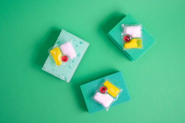 Bulaşık makineleri için jel kapsülleri ve süngerler, fotokopi makinesinin bulunduğu yerin yeşil ve sarı arka planında, bulaşık yıkama ile bulaşık makinesi arasında seçim