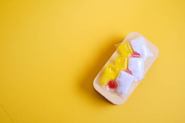 Bulaşık makineleri için jel kapsülleri ve süngerler, fotokopi makinesinin bulunduğu yerin yeşil ve sarı arka planında, bulaşık yıkama ile bulaşık makinesi arasında seçim