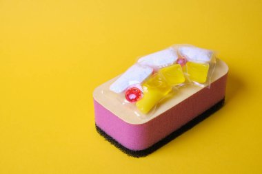 Bulaşık makineleri için jel kapsülleri ve süngerler, fotokopi makinesinin bulunduğu yerin yeşil ve sarı arka planında, bulaşık yıkama ile bulaşık makinesi arasında seçim