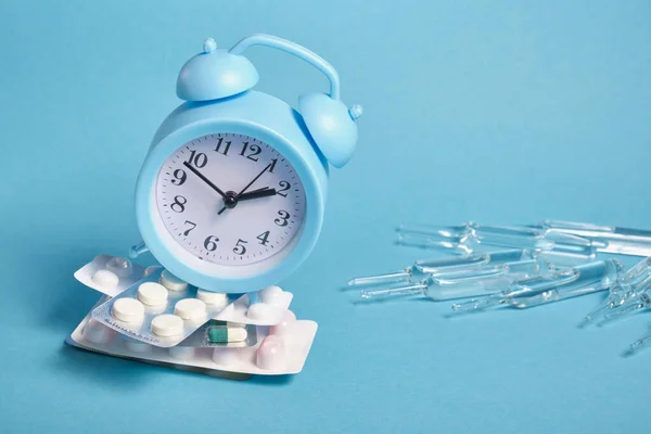 Grandes ampolas, relógio de alarme azul claro em uma pilha de embalagens de pílulas diferentes em um fundo azul, espaço de cópia, tomando medicamentos no conceito de tempo — Fotografia de Stock