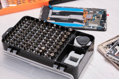 Siyah bir kutunun içindeki tornavida parçaları, eldivenler, bozuk akıllı telefonlar ve bir telefon ve tabletin camını değiştirmek için gerekli aletler.