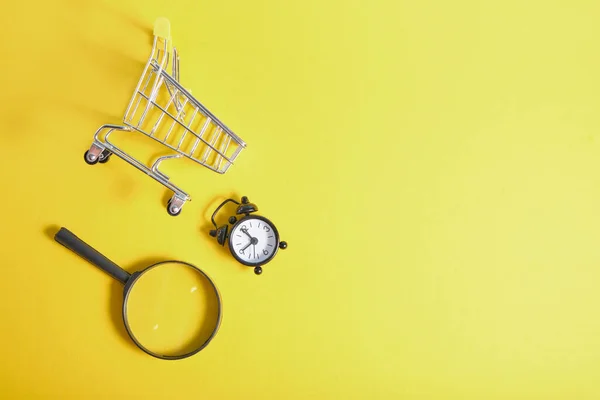 Magnifier Alarm Clock Miniature Shopping Basket Yellow Background Top View — Stock Photo, Image