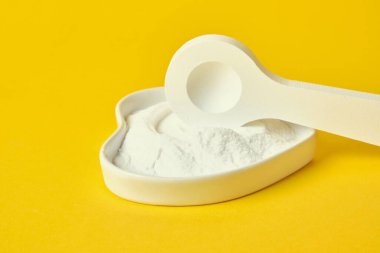 Küçük beyaz tahta oyuncak kaşık ve soda kalp şeklinde bir fincan altlığı sarı arka planda.