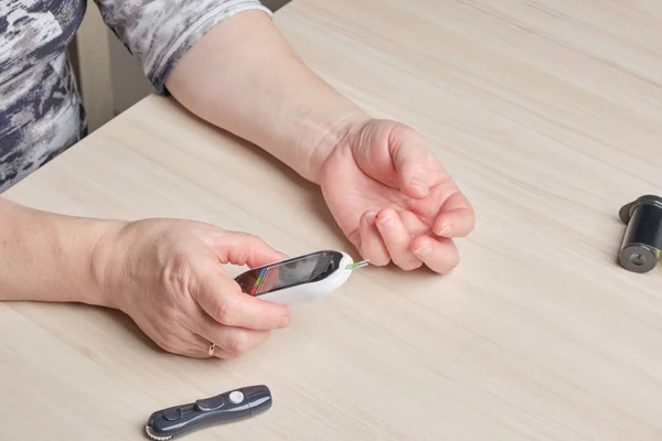 a senior woman with diabetes checks her blood sugar level with a glucose meter, a drop of blood on her finger, a high sugar level on the screen of a digital glucose meter