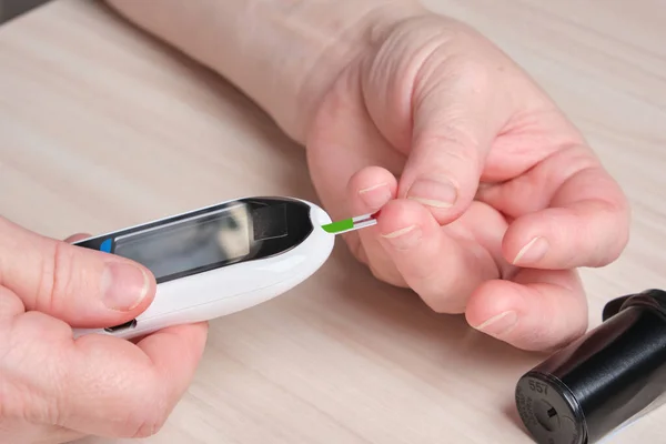 a senior woman with diabetes checks her blood sugar level with a glucose meter, a drop of blood on her finger, a high sugar level on the screen of a digital glucose meter