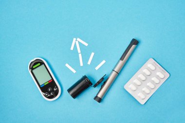 pills, glucose meter and syringe pen for injections of insulin on a blue background, test strips for measuring blood sugar in the shape of an arrow top view place copy clipart