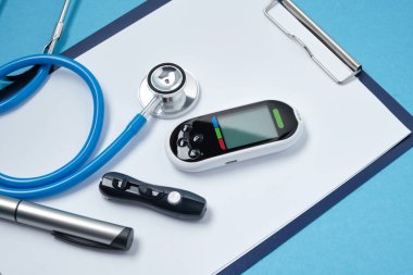 Beyaz boş kağıt, steteskop, glikoz ölçer, süs iğnesi ve mavi arka planda insülin bulunan şırınga, daibet günü konsepti, diyabet teşhisi