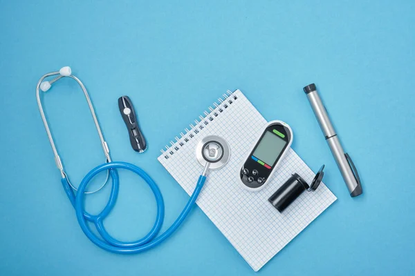 clean block with spring, stethoscope, glucose meter, lancet and syringe pen with insulin on a blue background, daibet day concept, diabetes diagnosis