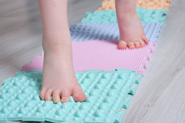 child massages feet with an orthopedic mat. prevention of flat feet and hallux valgus colored Orthopedic massage puzzle mats for the development of children.