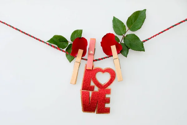 Red word LOVE  and rose on rope with clothespins, on a white  background
