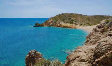 Işık dalgaları ve ufuk manzarası ile berrak mavi deniz kıyısında dağlar arasında Kumlu plaj