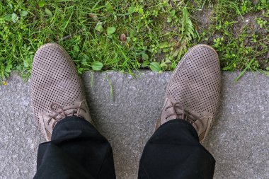 Mavi jeans ve yeşil ot ve gri kaldırım bir arka plan üzerinde kahverengi ayakkabı ayakları parçası.