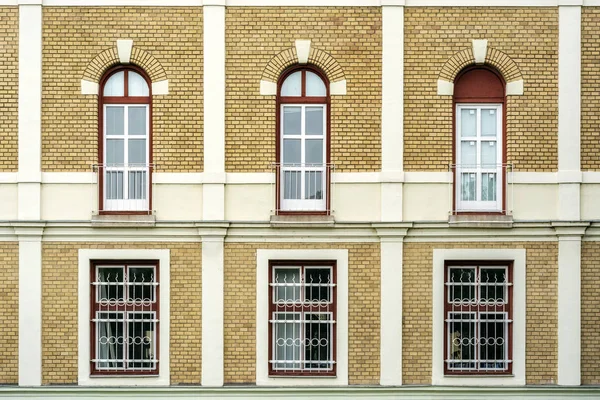 Six Windows against a wall of beige brick with arches and bars.