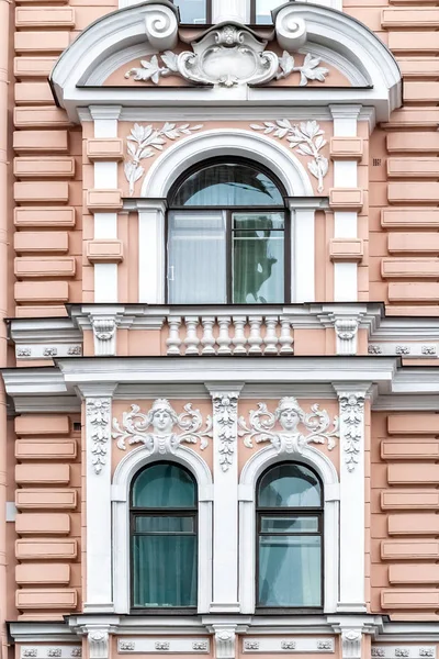Three arched windows with white stucco on the background of the wall in pink. From a series of windows of St. Petersburg.