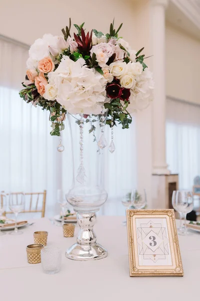 Magnificent, volume bouquets of flowers in high glass vases. Wedding flowers on tables for guests