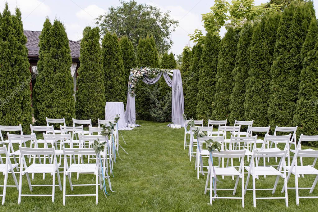 Wedding ceremony on a lawn under the open sky. A lot of white chairs and the arch for a wedding