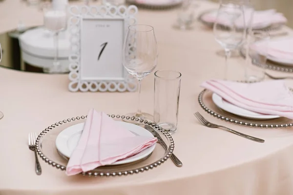 Placa branca e placa com contas de metal. Guardanapo de pano rosa em um prato de jantar e talheres — Fotografia de Stock