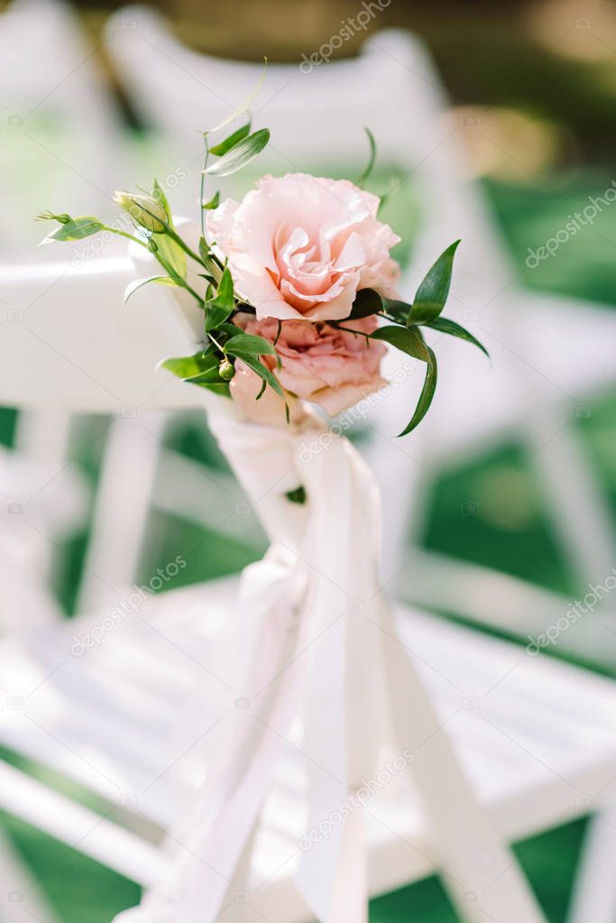 An elegant little bouquet of pink flowers and greens tied laterally on the back of a white chair
