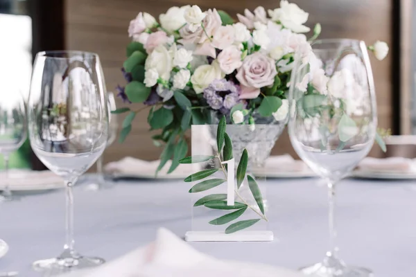 Champagne glasses, table number with number one and beautiful wedding flowers decorate the table at the wedding banquet.