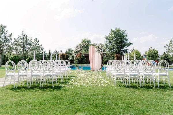 Łuk ślubny okrągły i przezroczyste krzesła z tworzywa sztucznego dla gości na zielonym trawniku w pobliżu podstawy — Zdjęcie stockowe