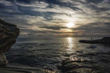 Günbatımı sırasında kayanın üzerinde duran bir adam. Güzel günbatımı manzara manzara. İlham verici kış Kıbrıs ve peyzaj fotoğraf. Kıbrıs, Şubat 2019