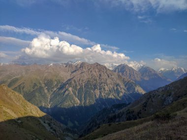 Almat şehri yakınlarındaki Kazakistan'da Tien Shan sisteminin Trans-Ili Alatau sıradağları. Yaz ortasında bulutların altında karla kaplı kayalık zirveler