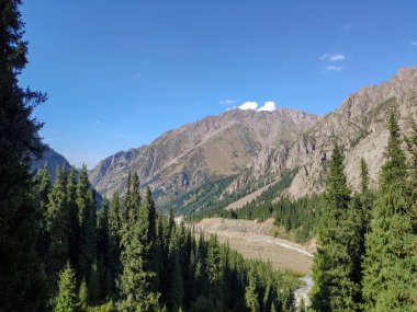 Almat şehri yakınlarındaki Kazakistan'da Tien Shan sisteminin Trans-Ili Alatau sıradağları. Yaz ortasında bulutların altında karla kaplı kayalık zirveler