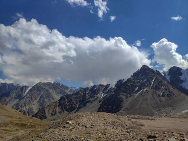 Almat şehri yakınlarındaki Kazakistan'da Tien Shan sisteminin Trans-Ili Alatau sıradağları. Yaz ortasında bulutların altında karla kaplı kayalık zirveler