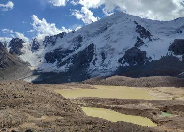 Almat şehri yakınlarındaki Kazakistan'da Tien Shan sisteminin Trans-Ili Alatau sıradağları. Yaz ortasında bulutların altında karla kaplı kayalık zirveler