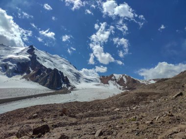 Almat şehri yakınlarındaki Kazakistan'da Tien Shan sisteminin Trans-Ili Alatau sıradağları. Yaz ortasında bulutların altında karla kaplı kayalık zirveler