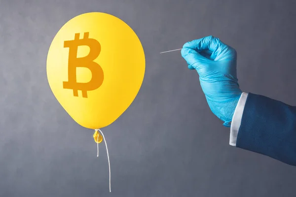 Bitcoin cryptocurrency symbol on yellow balloon. Man hold needle directed to air balloon. Concept of finance risk.