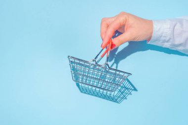 hand holding empty metal shopping basket. Concept of consumerism, shopping symbol. Copy space trend pastel color. Hard shadows, morning light.