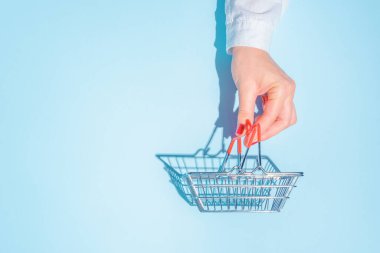 hand holding empty metal shopping basket. Concept of consumerism, shopping symbol. Copy space trend pastel color. Hard shadows, morning light.