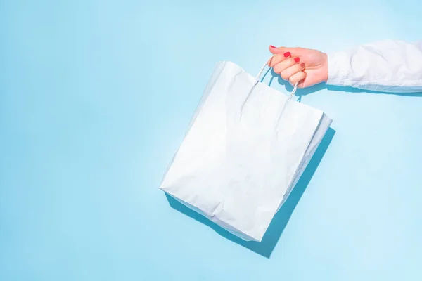 hand holding shopping paper bag. Concept of consumerism, shopping symbol. Copy space trend pastel color. Hard shadows, morning light.