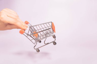 Boş metal alışveriş sepetini tutan el. Tüketim kavramı, alışveriş sembolü. Uzay eğilimi pastel rengini kopyala. Yumuşak gölgeler